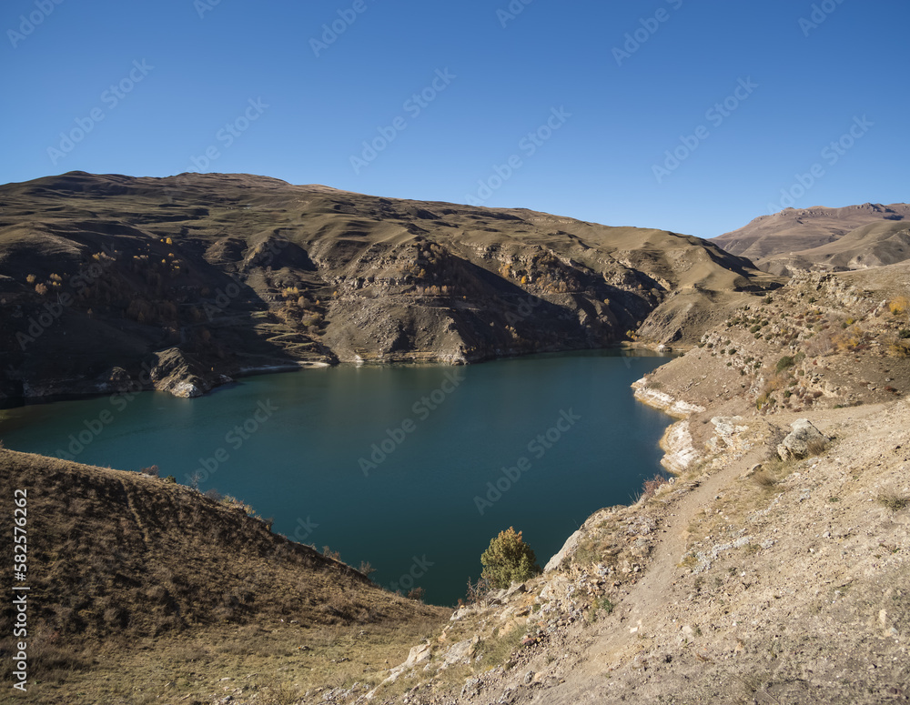 Mountain blue lake in the autumn mountains at the bottom of a valley with rocky shores on a sunny autumn morning, a cold lake in a mountainous area