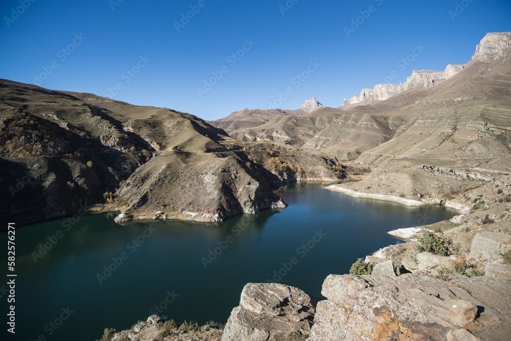Mountain blue lake in the autumn mountains at the bottom of a valley with rocky shores on a sunny autumn morning, a cold lake in a mountainous area