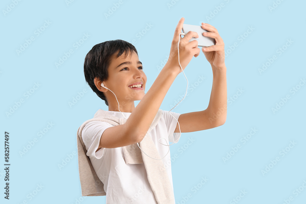 Little boy in earphones using mobile phone on blue background Little boy in earphones using mobile phone on blue background