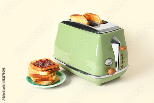 Bread slices in modern toaster and tasty toasts with jam on beige background