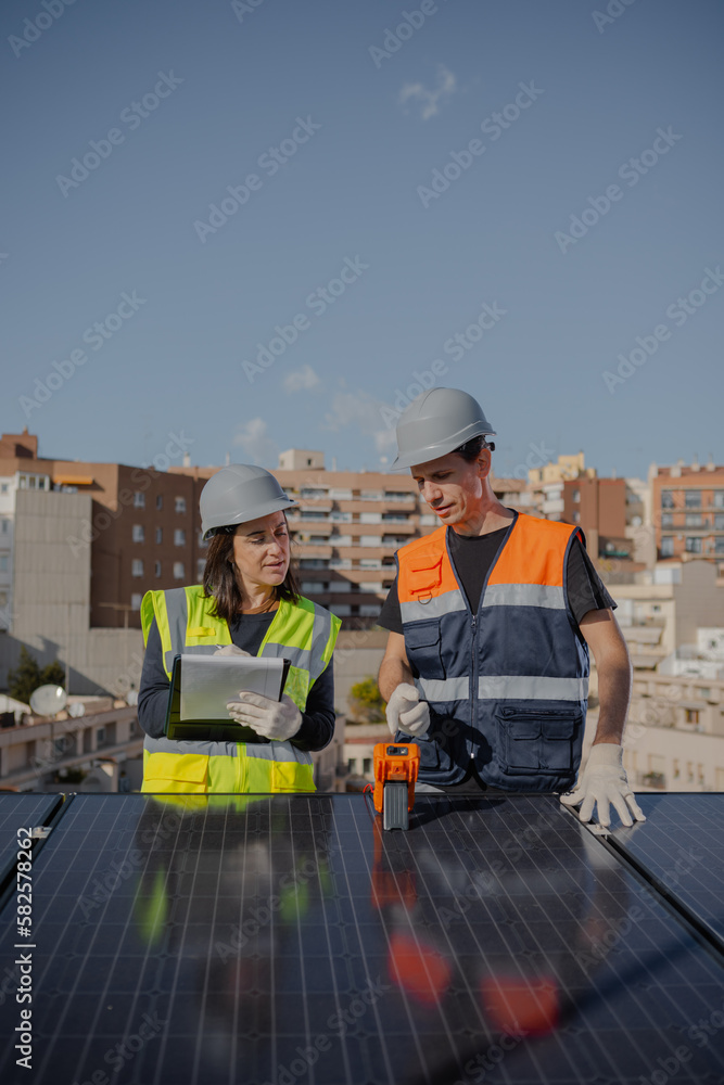 Teamwork testing urban Solar Panels with Multimeter and clipboard, man receiving instructions from female engineer for installation of photovoltaic system. Renewable energy. Vertical copy space. Teamwork testing urban Solar Panels with Multimeter and clipboard, man receiving instructions from female engineer for installation of photovoltaic system. Renewable energy. Vertical copy space.
