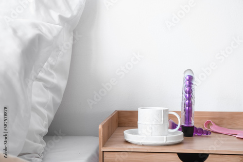 Vibrator with anal plug and cup of coffee on table in bedroom