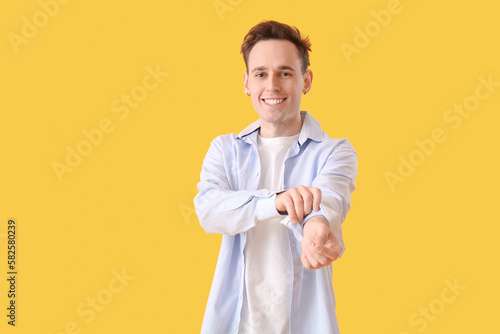 Young man rolling up his sleeve on yellow background