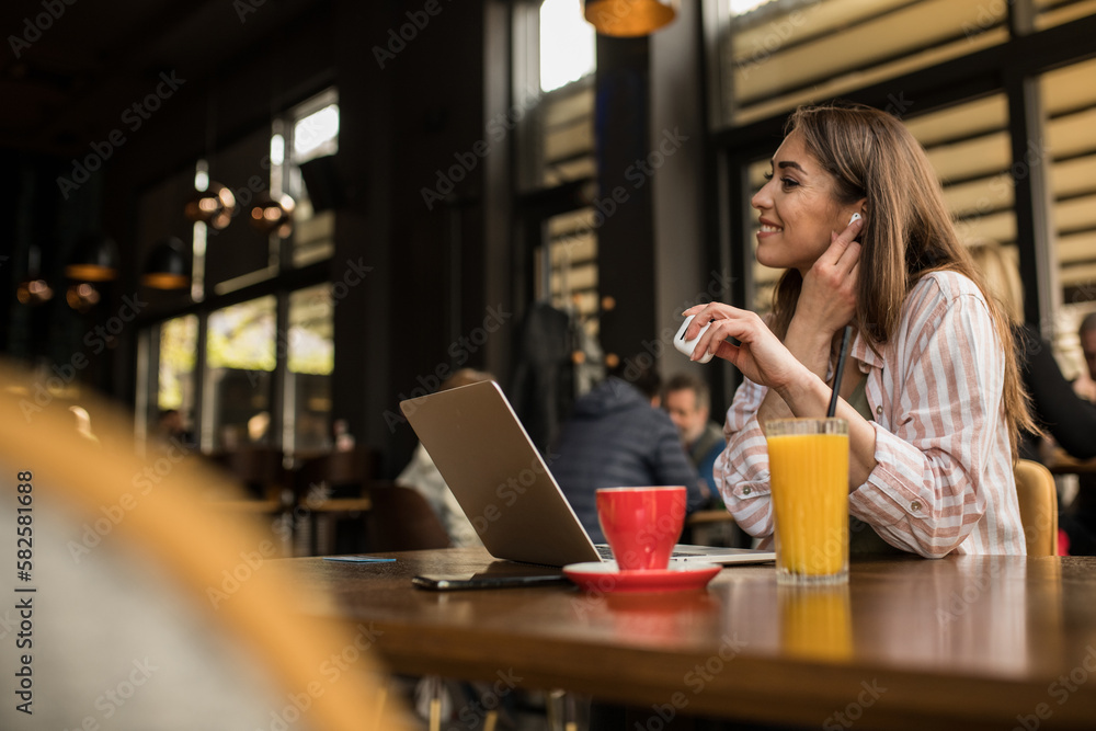 Woman putting in wireless earphones while working remotely from a restaurant Woman putting in wireless earphones while working remotely from a restaurant