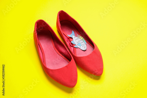 Female shoes with paper fish on yellow background. April Fools' Day celebration