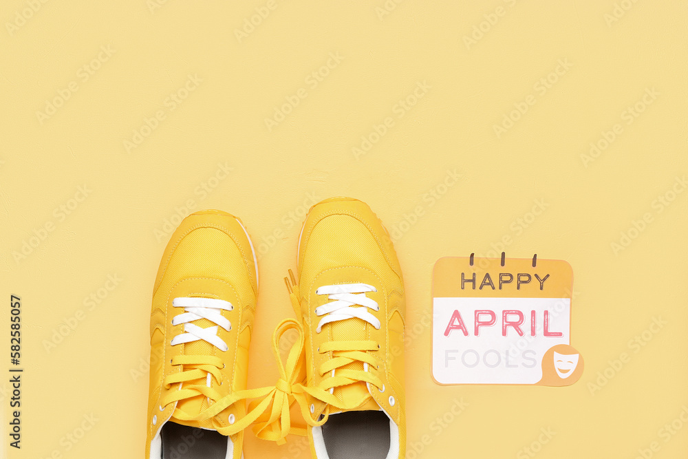 Paper with text HAPPY APRIL FOOLS and sneakers on yellow background Paper with text HAPPY APRIL FOOLS and sneakers on yellow background