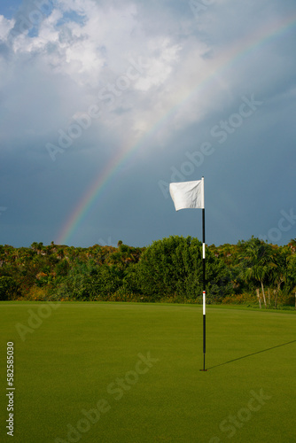Flag on green of golf course with dramatic sky and rainbow in background.