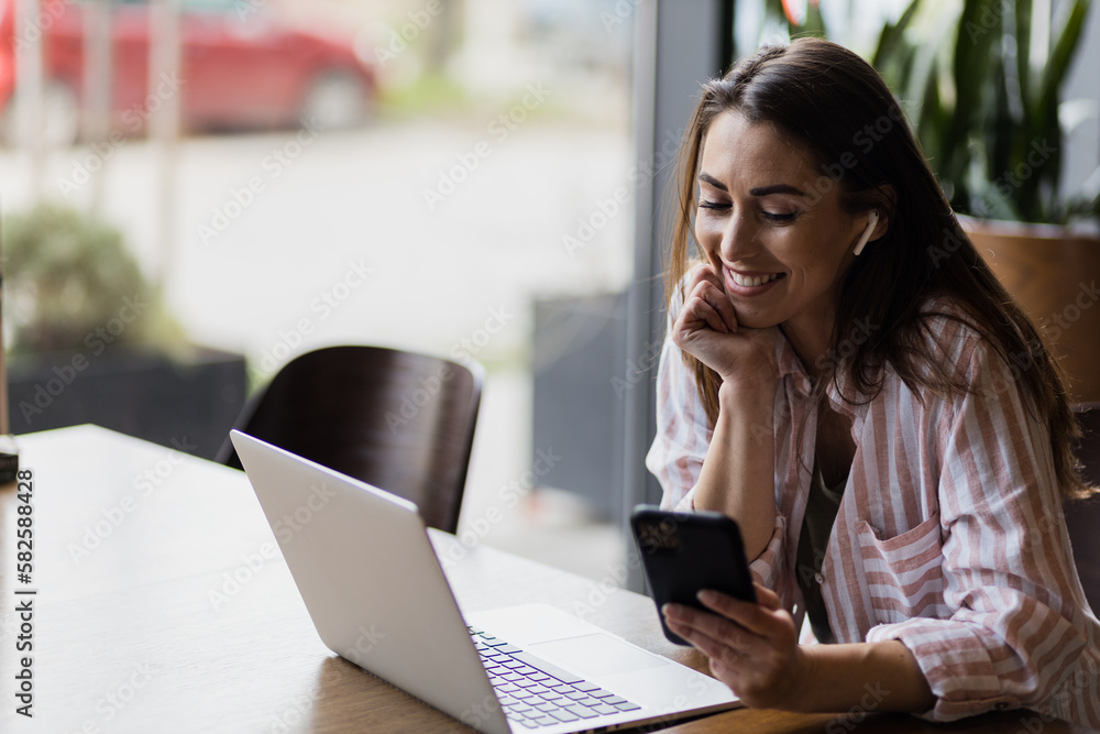 A businesswoman uses her phone for studying while using her laptop at a restaurant.
