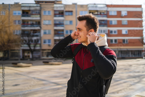 A young guy wearing wireless headphones or earbuds and using his phone outside in the city during the day 