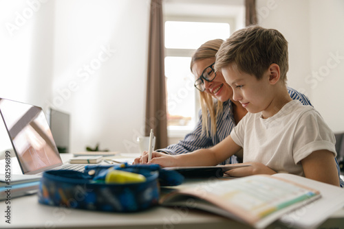 Happy mom and son doing homework and studying with laptop together. Home education photo