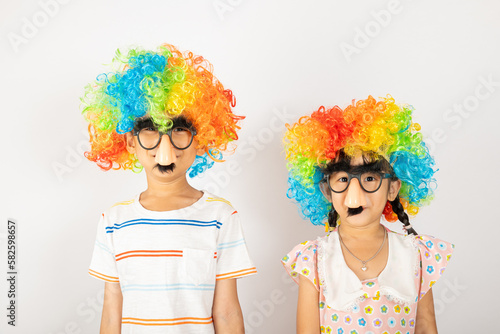 April Fool's Day. Two brothers funny kid boy and little girl clown wears curly wig colorful big nos and glasses and has mustache isolated on white background, Happy children festive decor