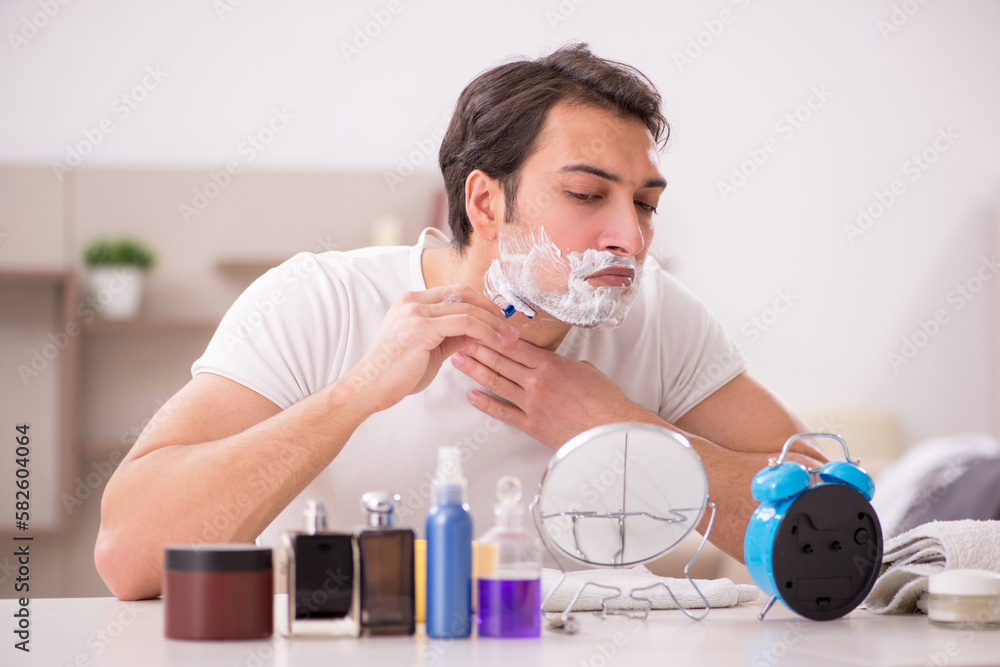 Young man shaving face at home