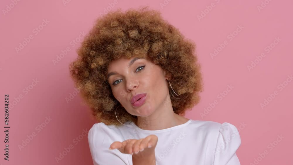 Portrait video of a wonderful girl with an afro hairstyle in a crisp white blouse against a pink background, she smiles and blows a kiss to the camera, copy space, high quality video Portrait video of a wonderful girl with an afro hairstyle in a crisp white blouse against a pink background, she smiles and blows a kiss to the camera, copy space, high quality video