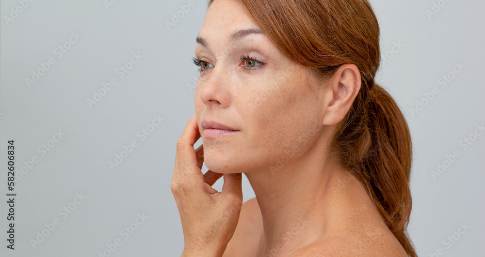 Portrait of middle aged woman with reddish hair holding hand on cheek looking at camera on gray background Portrait of middle aged woman with reddish hair holding hand on cheek looking at camera on gray background