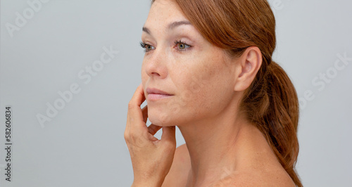 Fotografija Portrait of middle aged woman with reddish hair holding hand on cheek looking at