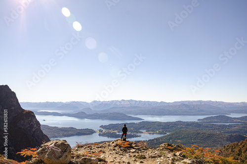 Mujer en la cima de una montaña apreciando el impactante paisaje de lagos, montañas y bosque despues de hacer tracking caminata escalada