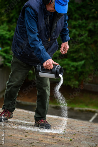 Senior man with a container of moss killer spreading the granules on a residential asphalt shake roof 