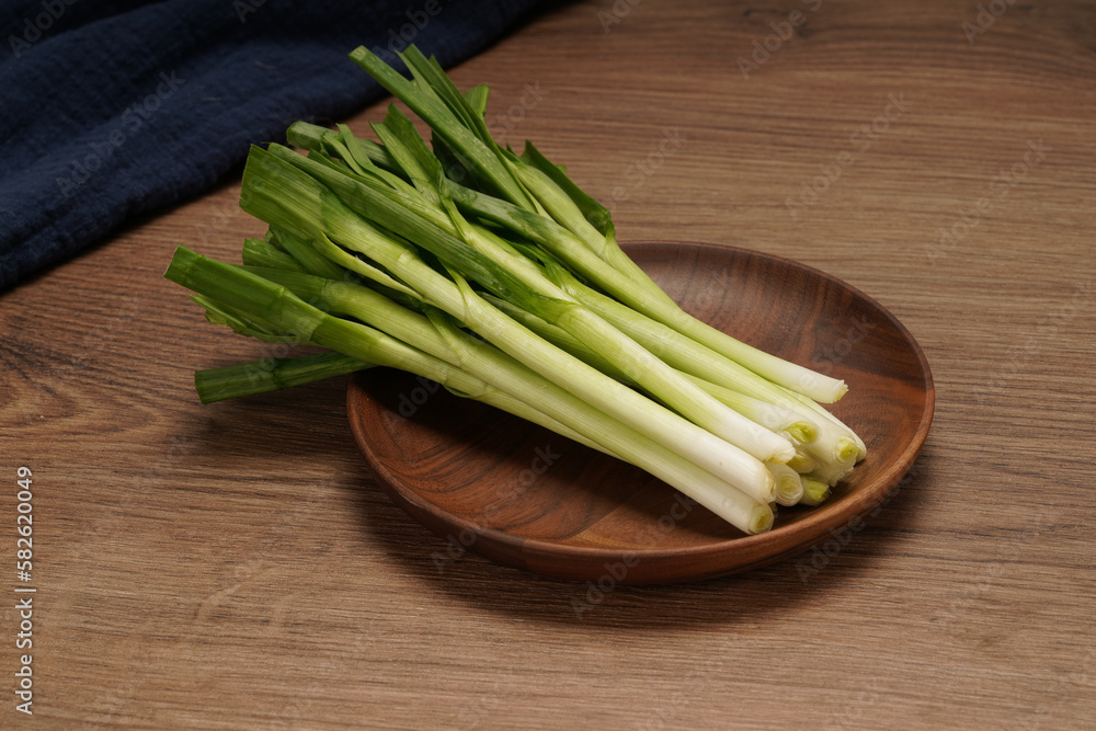 A pile of green onions on a wooden plate A pile of green onions on a wooden plate