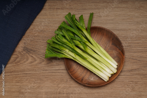 A pile of green onions on a wooden plate