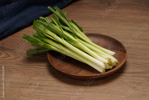 A pile of green onions on a wooden plate