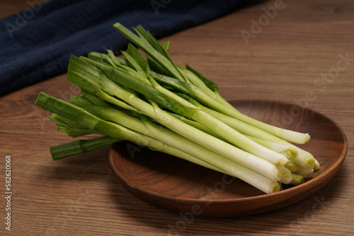 A pile of green onions on a wooden plate