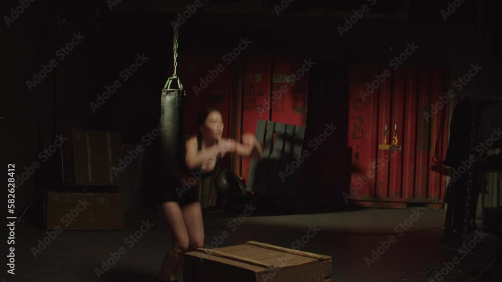 Active motivated sporty fit pretty Asian female doing box jump exercise, creating power and strength in lower body while practicing cross training in garage gym.