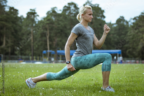 female runner doing lunge on green field, warm-up before athletics training