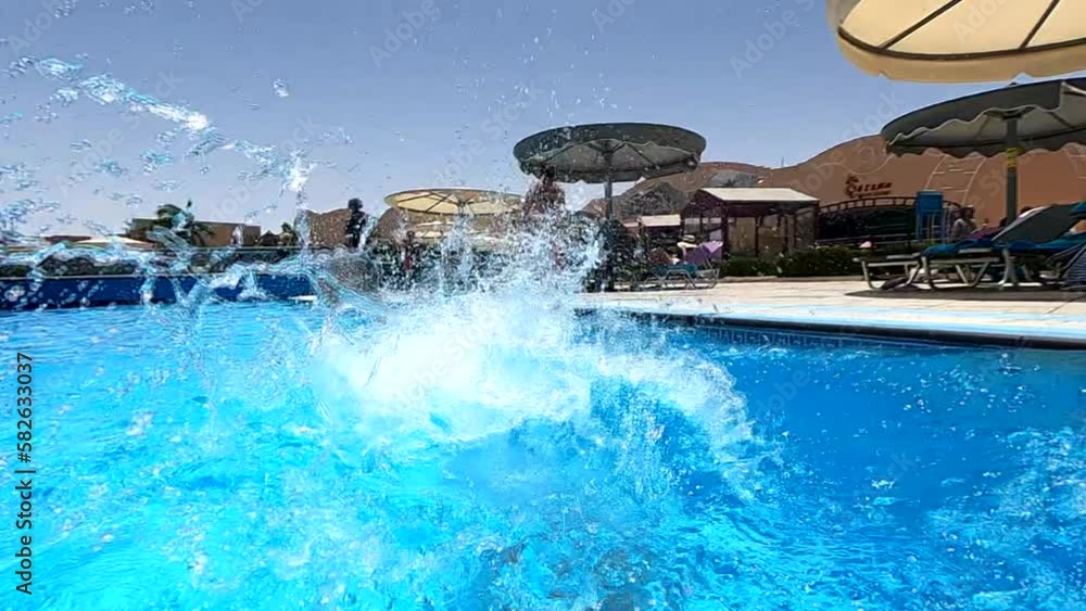 Happy little boy creates splashes in the pool, enjoying the cool water on a sunny day, the child is having fun in the pool, summer vacation Happy little boy creates splashes in the pool, enjoying the cool water on a sunny day, the child is having fun in the pool, summer vacation