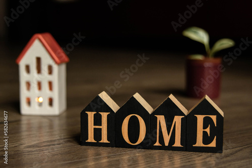 Wooden cubes with the inscription home on the wooden background. Plant in the pot.  House mock-up. The light is on in the window