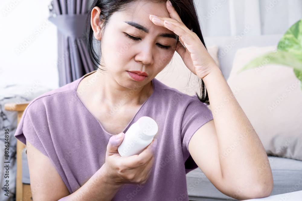 Asian woman have migraine headache hand holding a bottle of medicine Asian woman have migraine headache hand holding a bottle of medicine