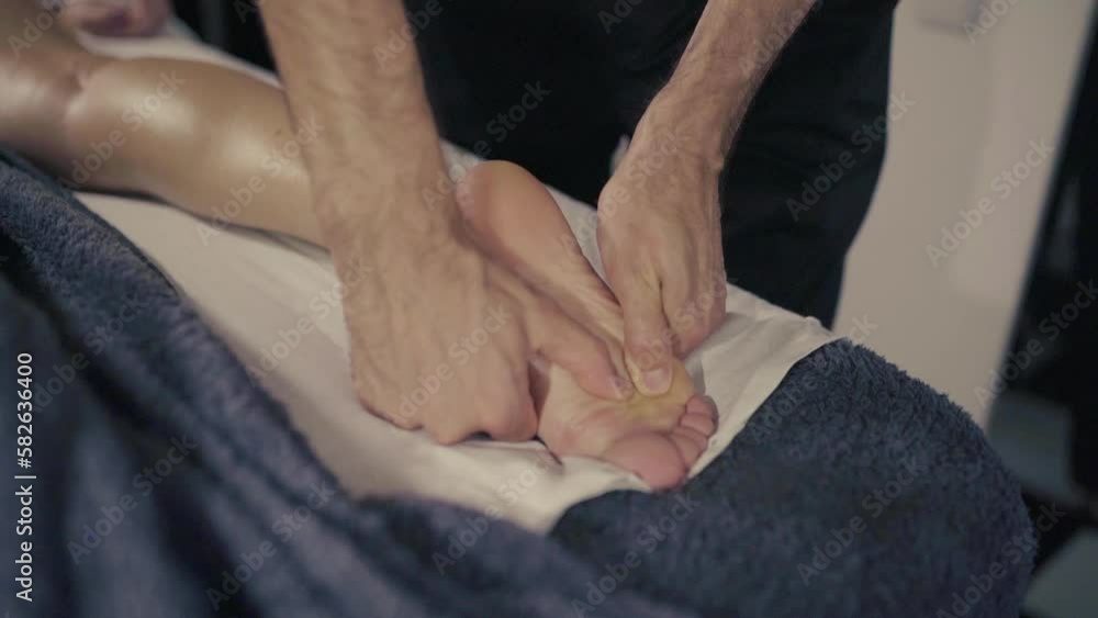 Young woman getting feet massage with oil by male masseur in luxury resort spa salon for body relaxation and skin care. Slow motion, close-up. Young woman getting feet massage with oil by male masseur in luxury resort spa salon for body relaxation and skin care. Slow motion, close-up.