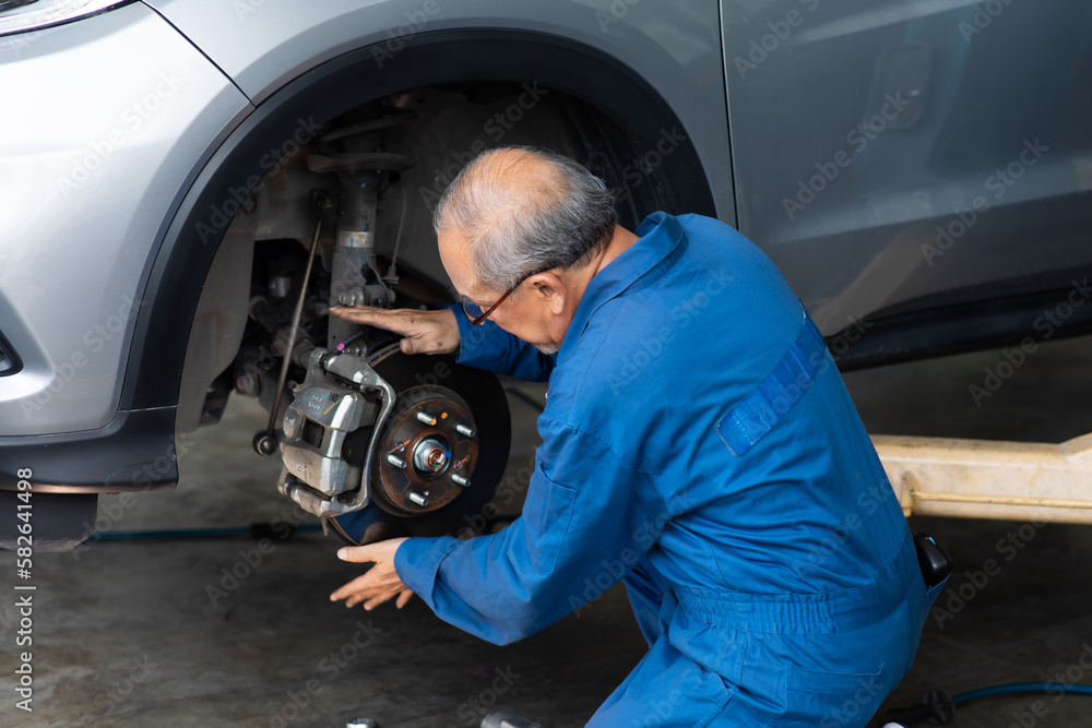Asian senior man mechanic changing car wheel at Car maintenance and auto service garage. Elderly male worker people