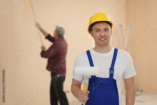 Worker holding paint roller in unfinished room. Painting walls