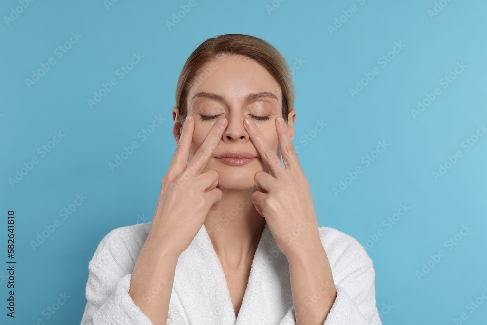 Woman massaging her face on turquoise background Woman massaging her face on turquoise background
