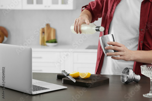 Man learning to make cocktail with online video on laptop at table in kitchen, closeup. Time for hobby