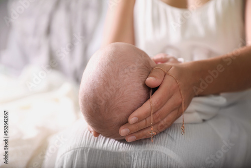 Mother holding newborn baby and Christian cross indoors, focus on hand