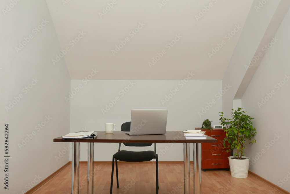 Stylish workplace with laptop and documents in attic room. Interior design