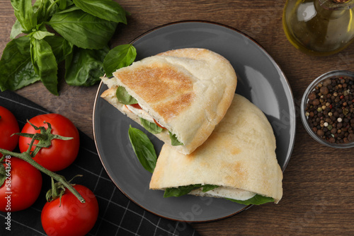 Delicious pita sandwiches with mozzarella, tomatoes and basil on wooden table, flat lay