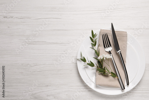 Stylish setting with cutlery and eucalyptus leaves on white wooden table, flat lay. Space for text