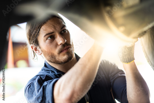 Hipster man mechanic working Under a Vehicle in a Car Service station. Expertise mechanic working in automobile repair garage. © NVB Stocker