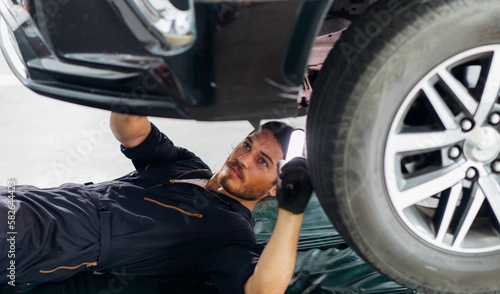 Hipster man mechanic working Under a Vehicle in a Car Service station. Expertise mechanic working in automobile repair garage.