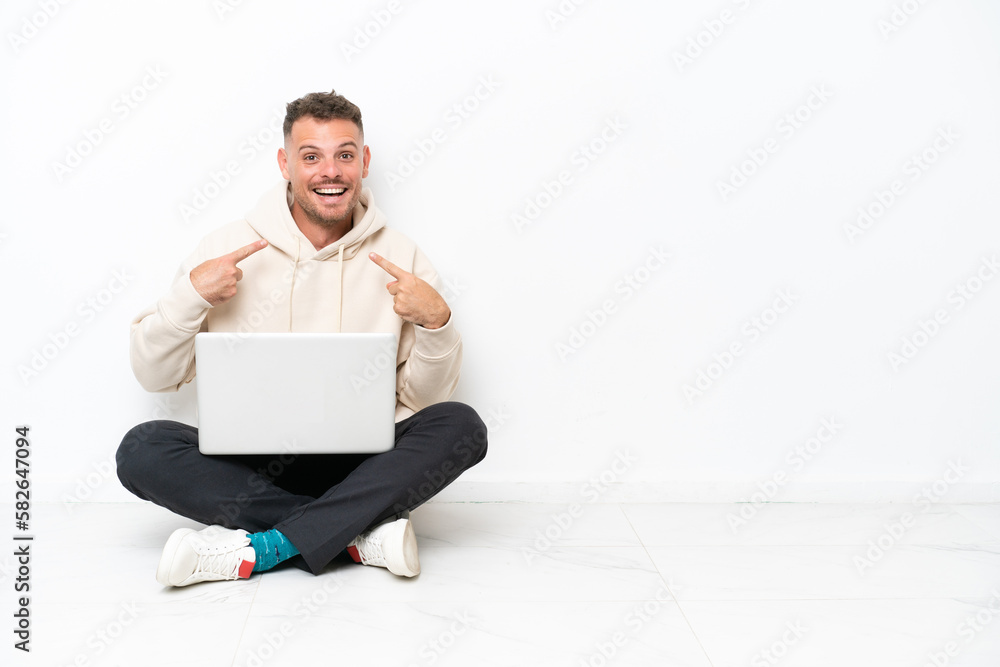 Young caucasian man with a laptop sitting on the floor isolated on white background with surprise facial expression