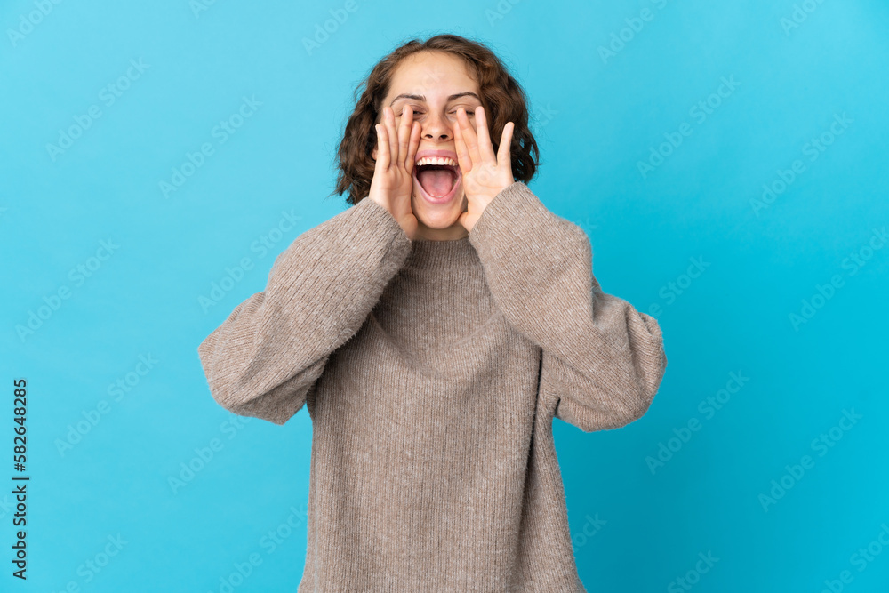 Young English woman isolated on blue background shouting and announcing something Young English woman isolated on blue background shouting and announcing something