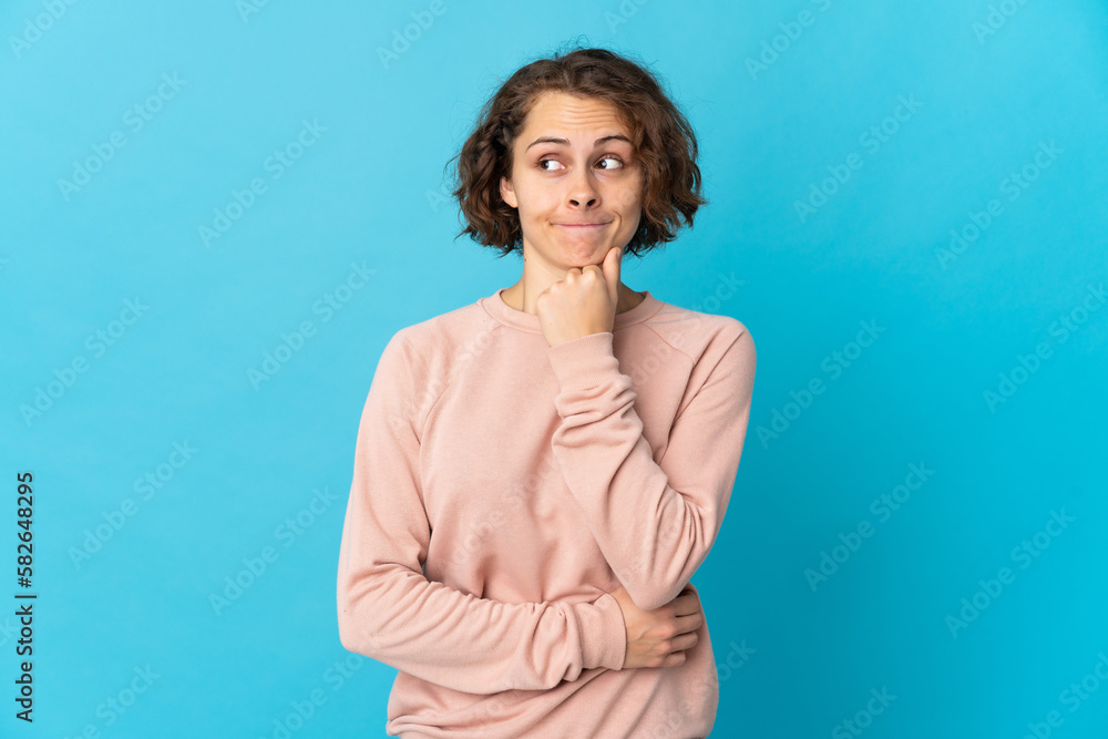 Young English woman isolated on blue background having doubts and thinking Young English woman isolated on blue background having doubts and thinking