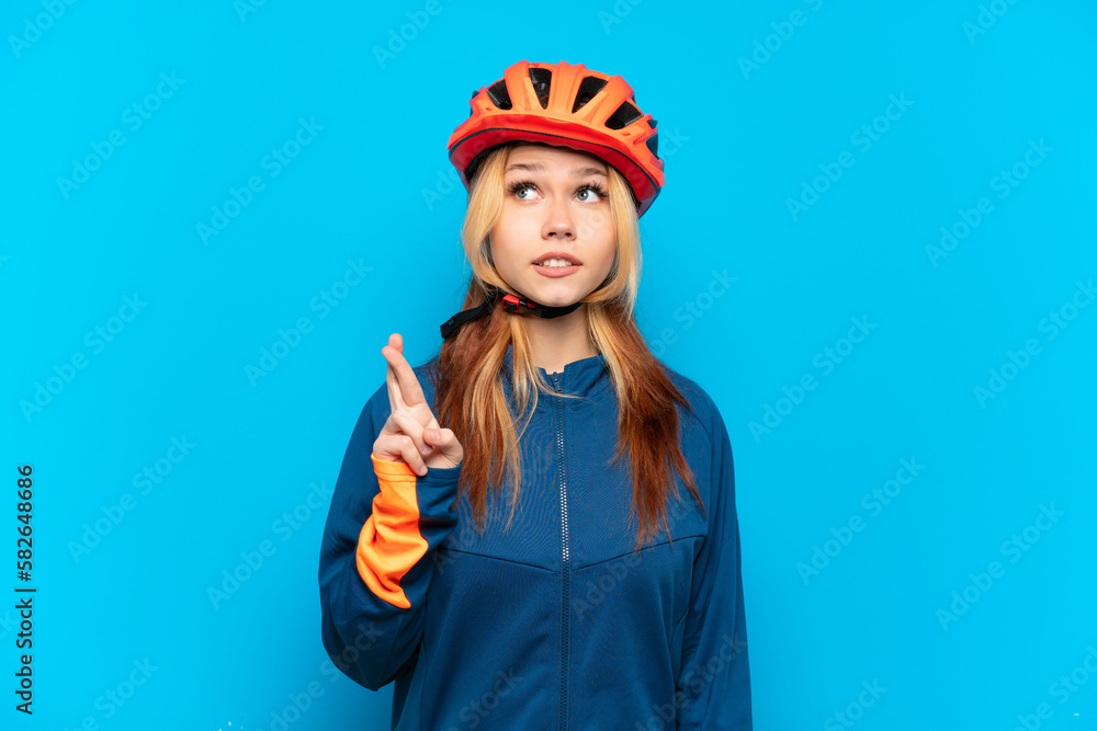 Young cyclist girl isolated on blue background with fingers crossing and wishing the best Young cyclist girl isolated on blue background with fingers crossing and wishing the best