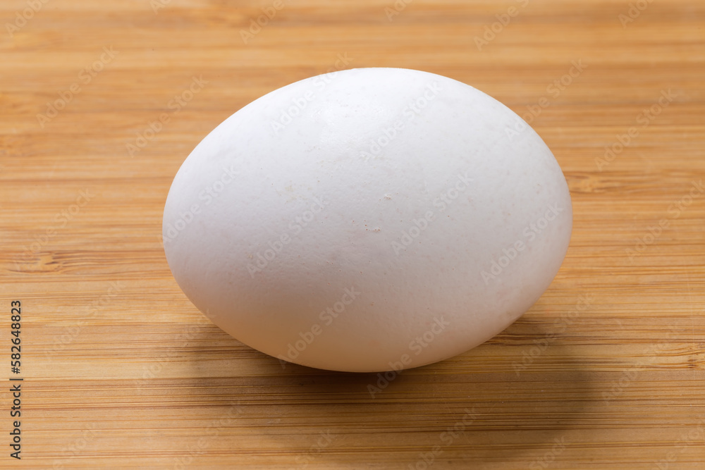 Whole white chicken egg illuminated from above on wooden surface Whole white chicken egg illuminated from above on wooden surface