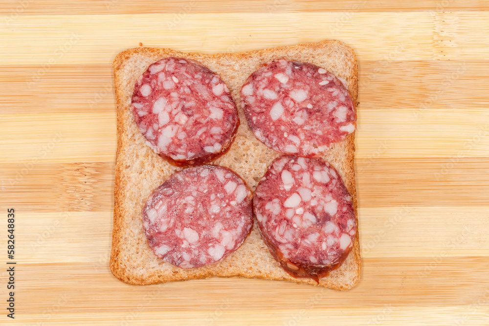 Open sandwich with dry-cured sausage on bamboo cutting board