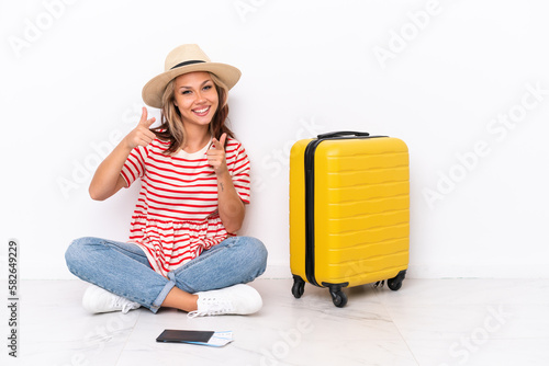 Young traveler girl sitting one the floor isolated on white background pointing to the front and smiling © luismolinero