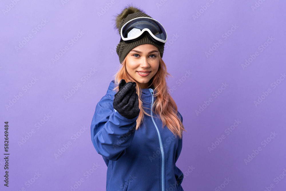 Skier teenager girl with snowboarding glasses over isolated purple background making money gesture