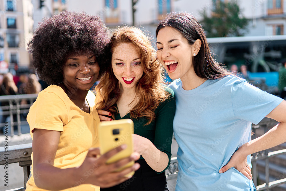 Obraz premium Curious and happy women sharing a mobile in the street